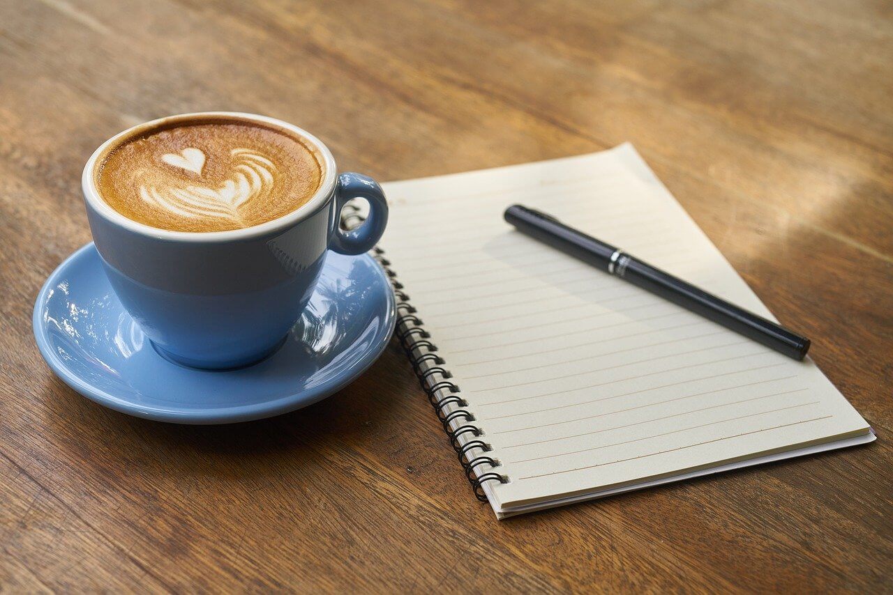 Káva na stole s zápisníkem a tužkou
